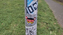 Metallpfahl mit verschiedenen Stickern, mittig ein feddit.org Sticker.